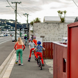Hoopla Kids riding their wheels down a Rongotai street one grey afternoon, wearing bright coloured clothes from the Hoopla Kids Stockroom
